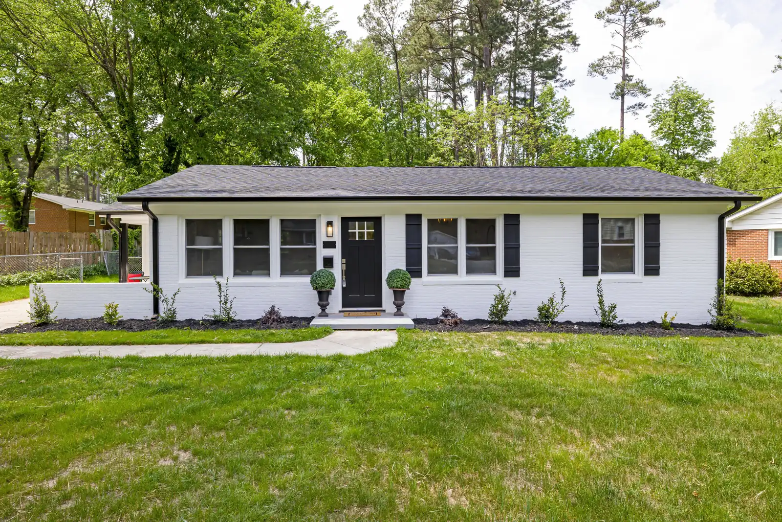 White painted brick ranch house with black shutters and a dark shingle roof