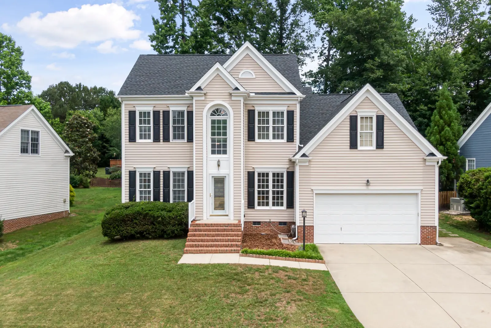 Two-story colonial home with beige vinyl siding, black shutters and an attached garage
