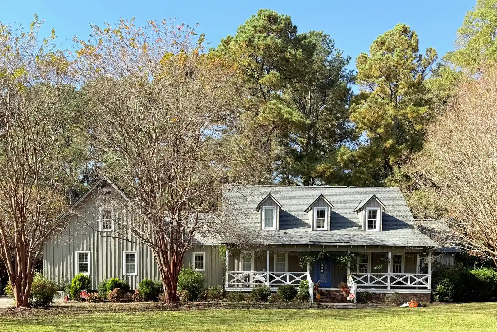 Cape Cod-style house with three dormers, a gray shingle roof and a covered front porch among trees